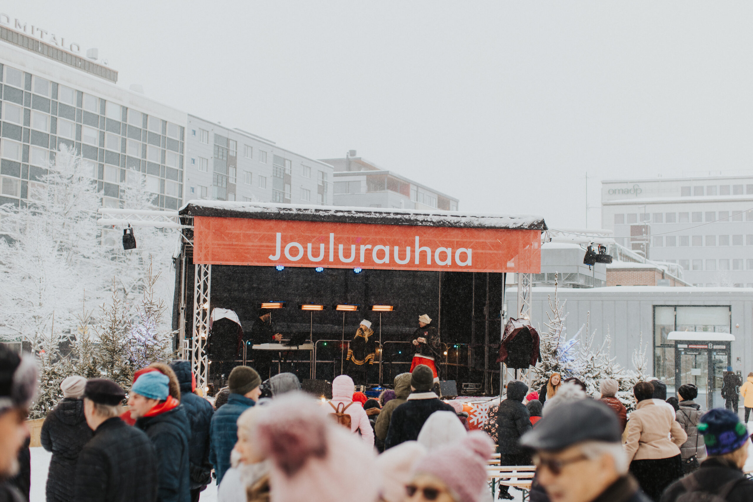 Kuva lahden Joulukylästä lavan suuntaan, jossa Joulukylän juontaja haastattelee esiintyjää. Kuvan etualalla näkyy yleisöä.